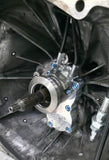A close-up of a metallic mechanical component, likely a transmission or differential part, installed inside a dark metal housing with visible bolts, shaft, and surrounding machinery parts.